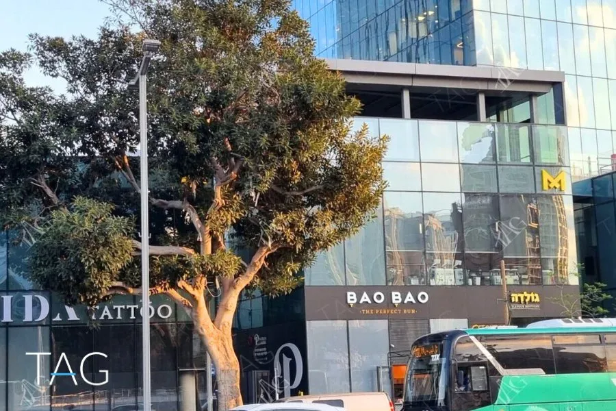קומת הקרקע של מגדל מידטאון, חנויות מאחורי חזית זכוכית, עץ גדול ואוטובוס עירוני ברחוב - תג נכסים