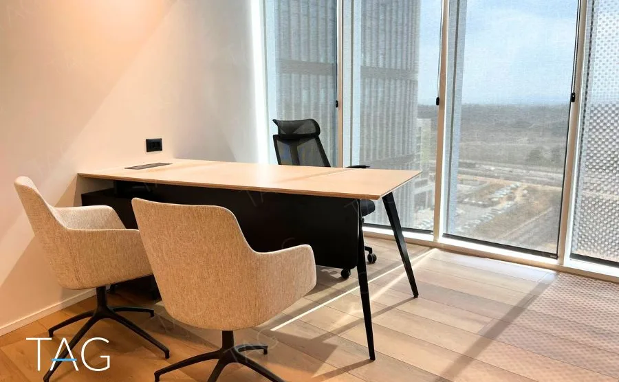 חדר מנהל בACRO BUSINESS CAMPUS עם שולחן עץ, כורסאות ונוף מהחלון הפינתי - תג נכסים