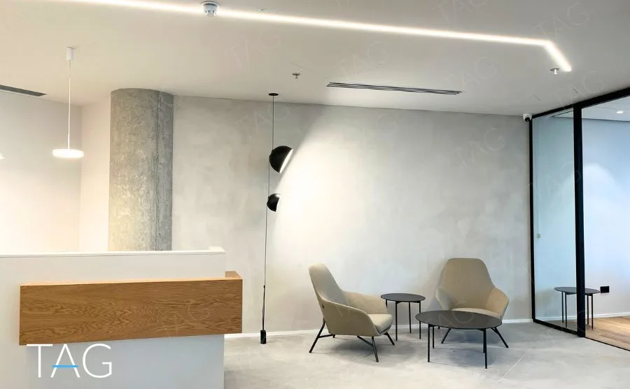 עמדת קבלה בACRO BUSINESS CAMPUS עם דלפק עץ בהיר, קיר טיח מרוח וכורסאות אפורות - תג נכסים