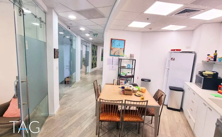 מטבחון ופינת אוכל במשרד במגדל רוטשילד 3 עם מחיצת זכוכית, מקרר ושולחן עץ