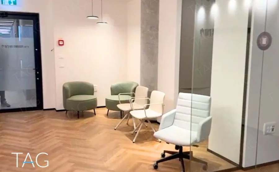 פינת המתנה בACRO BUSINESS CAMPUS עם כורסאות ירוקות, פרקט אדרה ותאורה תלויה - תג נכסים