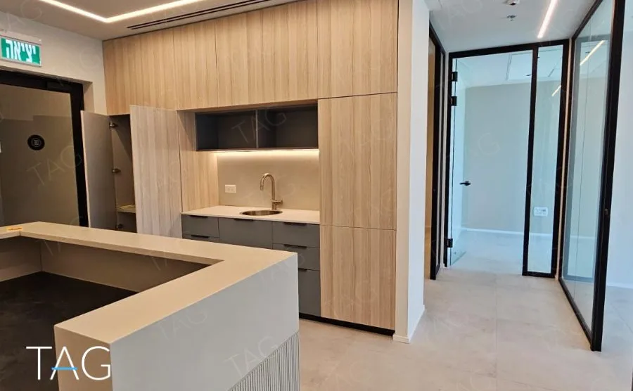 מטבחון בACRO BUSINESS CAMPUS עם ארונות עץ בהיר, דלפק אבן ומחיצות זכוכית - תג נכסים