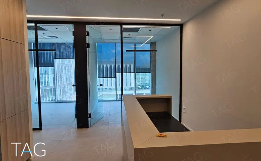 חלל משרדי בACRO BUSINESS CAMPUS עם דלפק עץ, מחיצות זכוכית שחורות ותאורה שקועה - תג נכסים