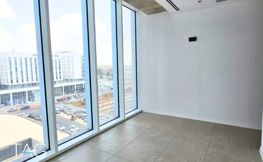 חדר משרד בACRO BUSINESS CAMPUS עם חלון פינתי מרצפה לתקרה ואריחים אפורים - תג נכסים