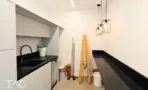 מטבחון משרדי בACRO BUSINESS CAMPUS עם ארונות לבנים, משטח שחור ותאורה תלויה - תג נכסים