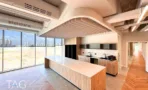 מטבח משרדי בACRO BUSINESS CAMPUS עם אי עץ מרכזי, תקרת סנפירים ונוף מהחלון - תג נכסים
