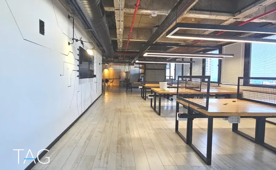 מסדרון עם תקרה חשופה וצנרת אדומה לאורך עמדות העבודה במשרד להשכרה באזור רוטשילד תל אביב