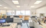 קומת עבודה פתוחה עם עמדות מחשב לאורך קיר החלונות ונוף עירוני רחב במגדל על