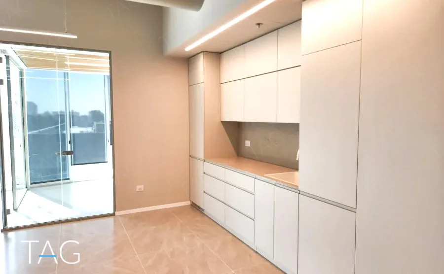 מטבחון בACRO BUSINESS CAMPUS עם ארונות לבנים גבוהים ויציאה למרפסת - תג נכסים