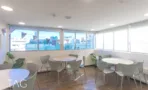אזור אוכל עם שולחנות עגולים וחלונות פינתיים במשרד להשכרה באזור רוטשילד