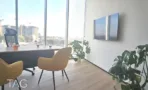 חדר עבודה בACRO BUSINESS CAMPUS עם שולחן, כורסאות, צמחייה ומסך על הקיר - תג נכסים