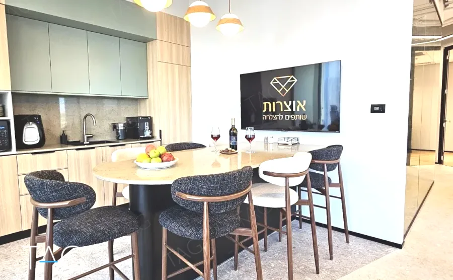 מטבח משרדי בACRO BUSINESS CAMPUS עם ארונות ירוקים, שולחן עגול וכיסאות בר - תג נכסים