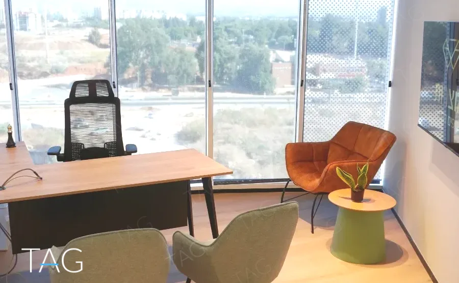 חדר מנהל בACRO BUSINESS CAMPUS עם שולחן עץ, כורסה כתומה ונוף לשטח פתוח - תג נכסים