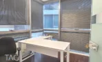 חדר פינתי במשרד במגדל רוטשילד 3 עם שני קירות חלונות עם תריסים, שולחן לבן ורצפת עץ כהה