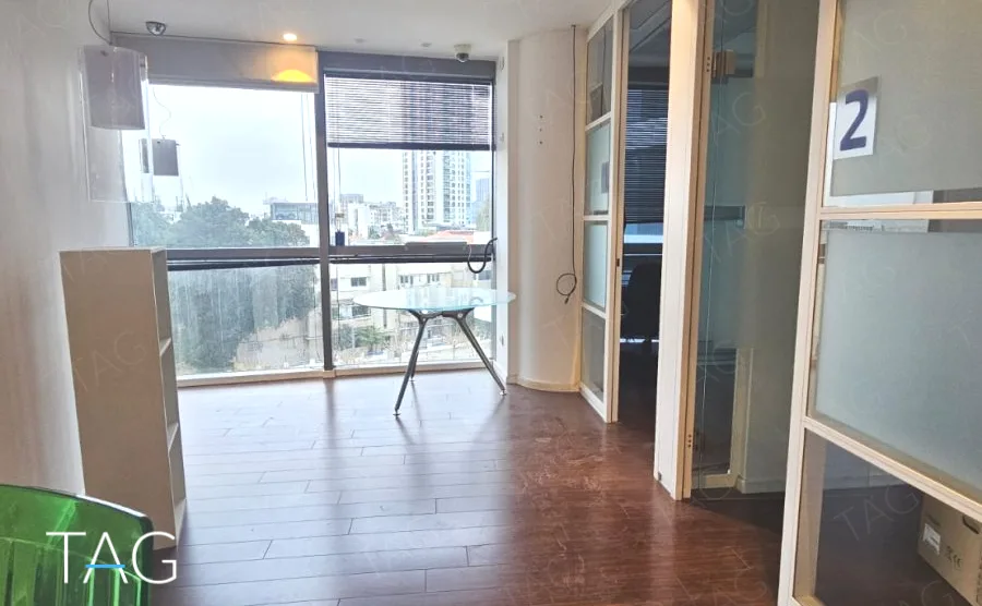 חדר במשרד במגדל רוטשילד 3 עם זיגוג רחב, מחיצות זכוכית, רצפת עץ ונוף לבנייה נמוכה ולמגדל סמוך