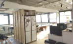 מטבחון המשרד להשכרה במגדל המאה, עם יחידת אחסון מעץ, מקרר גדול ודלפק בר גבוה מול החלונות