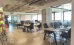 אזור אופן ספייס במשרד להשכרה במגדל המאה, עם שורות עמדות עבודה, תקרת בטון חשופה וחלונות לכל אורך הקיר