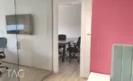 חדר עבודה קטן מאחורי מחיצת זכוכית במשרד להשכרה במגדל המאה, עם מסך תלוי על הקיר וקיר מג'נטה