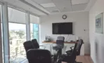 חדר ישיבות עם מסך תלוי ושולחן זכוכית מול חלון עירוני במשרד 170 מ