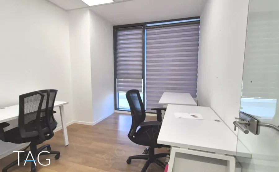 משרד להשכרה 360 מ״ר במגדלי אלון, חדר עבודה עם שני שולחנות לבנים וכיסאות שחורים ליד החלון