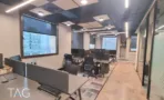 עמדות עבודה במשרד להשכרה בבית עוז ברמת גן, תקרה אקוסטית כהה עם תאורת פס וחלון לנוף מגדלי האזור - תג נכסים