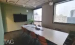 חדר ישיבות במשרד להשכרה בבית עוז ברמת גן, שולחן לבן ארוך וכיסאות בגוון חמרה מול חלון לנוף העיר - תג נכסים