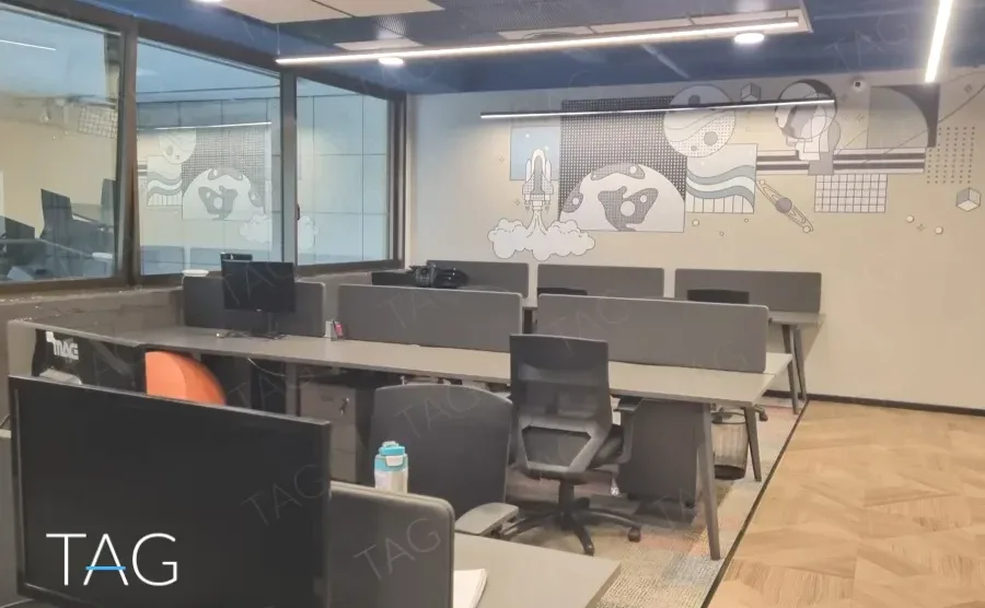 חלל עבודה פתוח במשרד להשכרה בבית עוז ברמת גן, שורות עמדות עם מחיצות ואיור קיר על מחיצת הזכוכית - תג נכסים