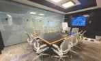 חדר ישיבות מוקף זכוכית עם שולחן ארוך, כיסאות משרדיים ומסך על הקיר, תקרה כהה עם פאנל תאורה - משרד 890 מר, אריה שנקר מרכז גב ים הרצליה - תג נכסים