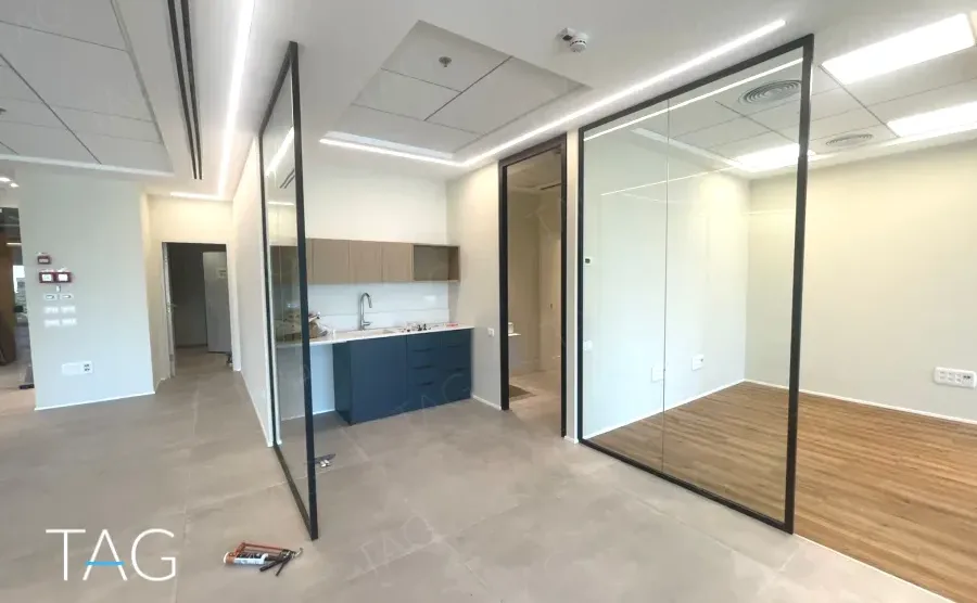 מטבחון כחול ומחיצות זכוכית על רצפת פרקט במשרד במגדל אייקון