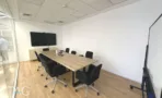 חדר ישיבות עם שולחן עץ ארוך ומסך על הקיר במשרד להשכרה ליד רכבת השלום - תג נכסים