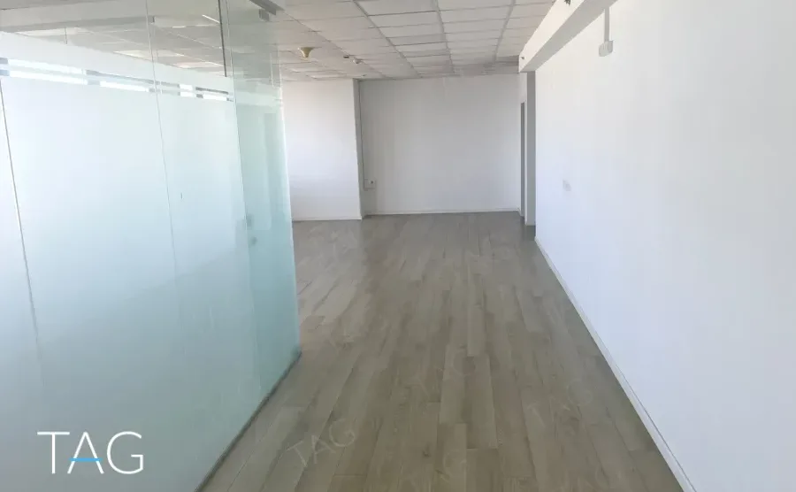 חלל ריק עם מחיצת זכוכית לכל האורך ופרקט בהיר במשרד במגדל שלום מאיר