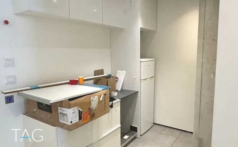 מטבחון בACRO BUSINESS CAMPUS עם ארונות לבנים, מקרר משולב ועמוד בטון - תג נכסים