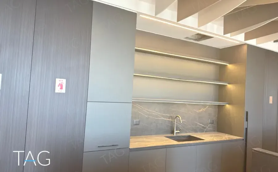 מטבח משרדי בACRO BUSINESS CAMPUS עם חיפוי עץ כהה, מדפים מוארים ומשטח אבן - תג נכסים