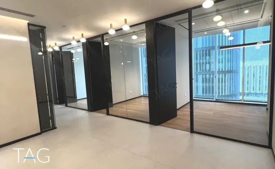 חלל משרדי בACRO BUSINESS CAMPUS עם חדרי זכוכית, תאורה תלויה ונוף עירוני - תג נכסים