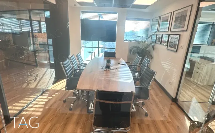 חדר ישיבות במשרד בבית אמפא הרצליה עם שולחן עץ אליפטי, כיסאות עור שחורים וקיר תמונות ממוסגרות - תג נכסים