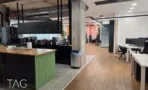 אי מטבח בגוון ירוק במשרד בבית אמפא הרצליה, לצד עמוד בטון וחלל עבודה פתוח - תג נכסים