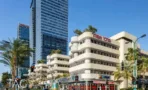 בית מרכז אשדר ביגאל אלון תל אביב במבט מהרחוב, שילוט המרכז בחזית ומגדלי זכוכית ברקע - תג נכסים