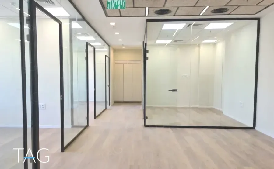 משרד בגמר מלא במגדל אייקון, פרקט בהיר ומחיצות זכוכית במסגרות שחורות