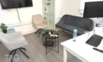 פינת קבלה עם ספה אפורה ומסך תלוי במשרד להשכרה ברוטשילד - תג נכסים