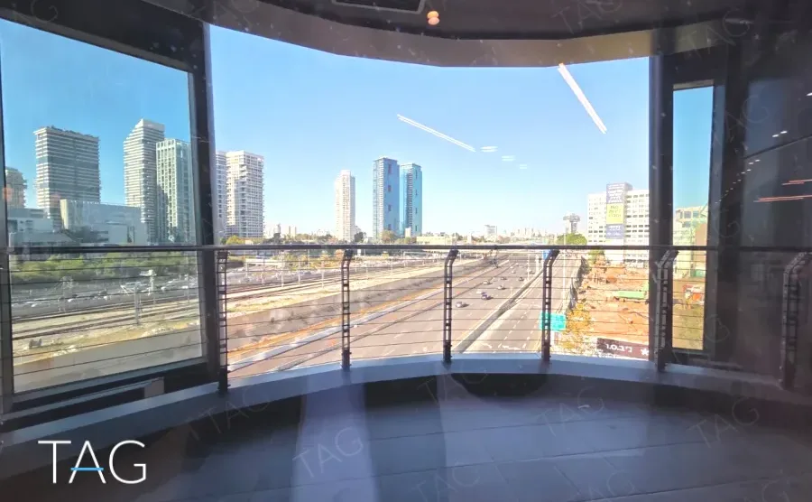 מרפסת מעוגלת במגדל אייקון עם מעקה מתכת, נוף אל נתיבי איילון והמסילה