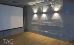 חדר הקרנה במשרד להשכרה ברחוב אחד העם תל אביב, מסך לבן וגופי תאורה על קיר בטון כהה - תג נכסים