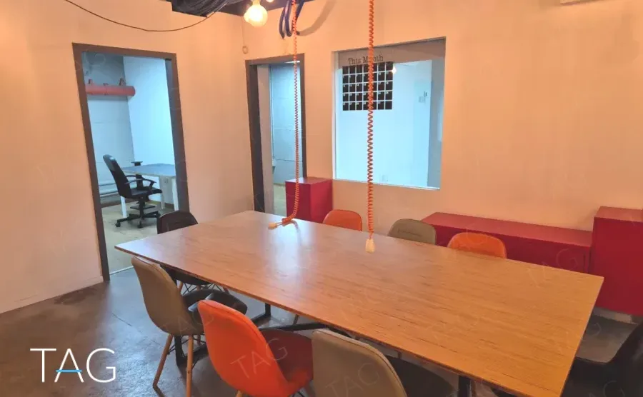 חדר ישיבות במשרד להשכרה ברחוב אחד העם תל אביב, שולחן עץ ארוך, כיסאות צבעוניים וקירות אפרסק - תג נכסים
