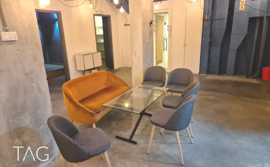 חלל פתוח במשרד להשכרה ברחוב אחד העם תל אביב, כורסה כתומה, שולחן זכוכית ועמודי בטון - תג נכסים