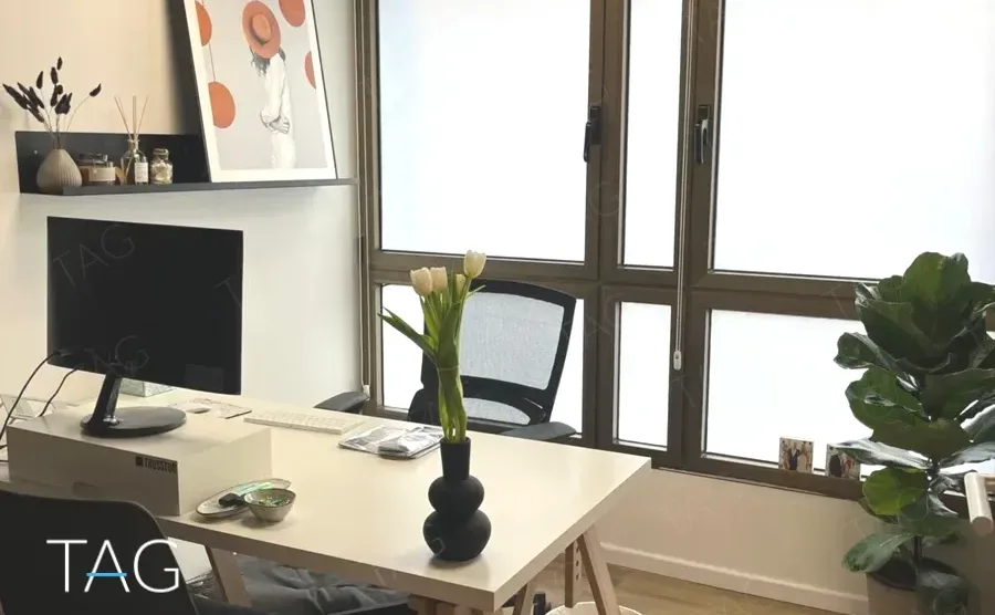 חדר עבודה בהשכרת משרד בשדרות רוטשילד תל אביב, שולחן לבן ליד חלון עץ רחב וצמחייה - תג נכסים