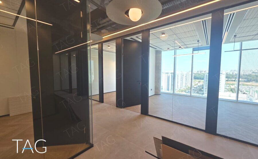 חלל משרדי בACRO BUSINESS CAMPUS עם מחיצות זכוכית, תאורה מעוצבת ונוף עירוני - תג נכסים