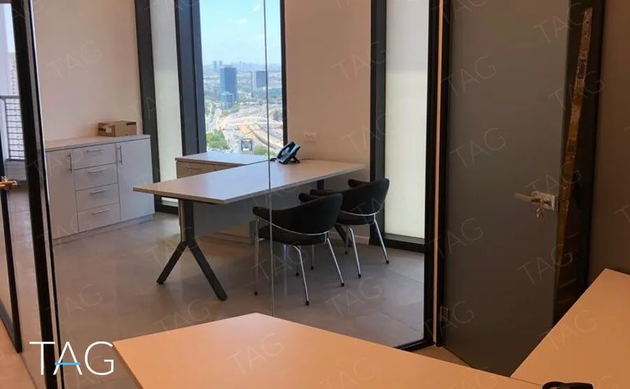 חדר עבודה מאחורי מחיצת זכוכית עם שולחן לבן, כיסאות שחורים וחלון פנורמי