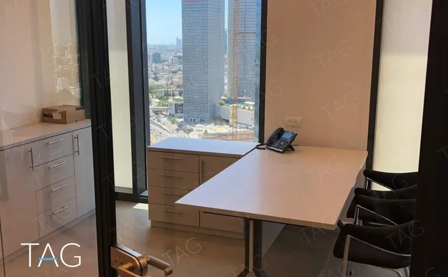 חדר עבודה מבעד לדלת זכוכית, עם שולחן בצורת L וחלון פנורמי הצופה אל מגדלי העיר