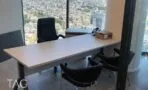 חדר עם שולחן עבודה, כיסא מנהלים וכיסאות אורח מול חלון רצפה תקרה הצופה לעיר