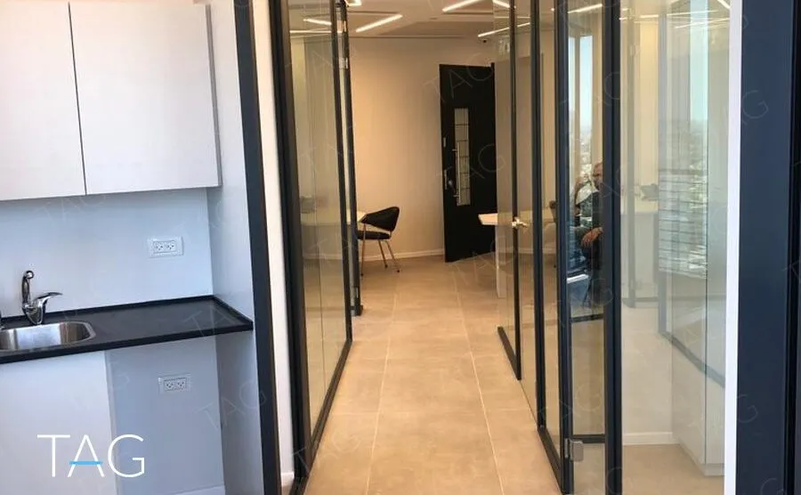 מסדרון פנימי עם רצפת אריחים בהירה, פינת כיור עם משטח שחור ומחיצות זכוכית
