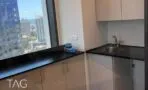 מטבחון עם משטח עבודה שחור, כיור נירוסטה, ארונות בהירים וחלון עם נוף לעיר